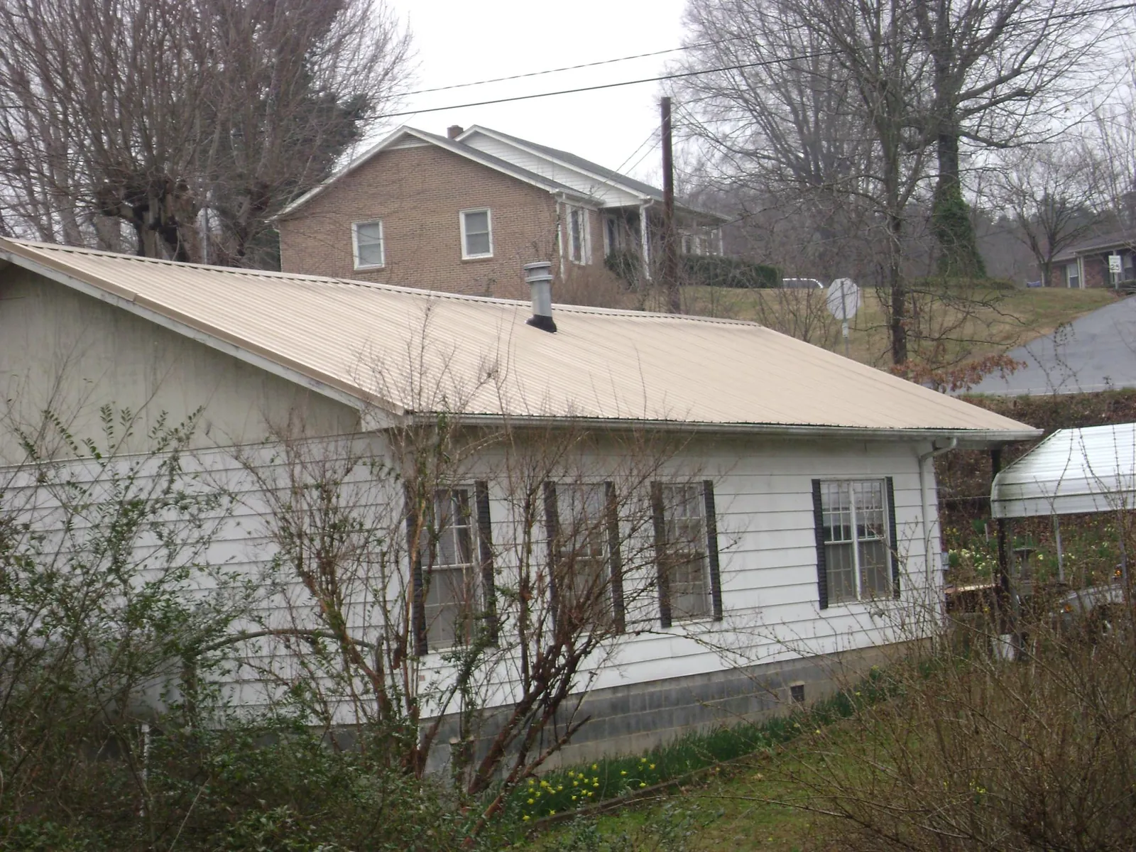 Tan metal roof on a white sided house set into a hillside — Commercial Roofing by Roofing Brothers in Grantville